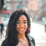 Attractive young woman with curly hair and eyeglasses smiling on a sunny day in the city.